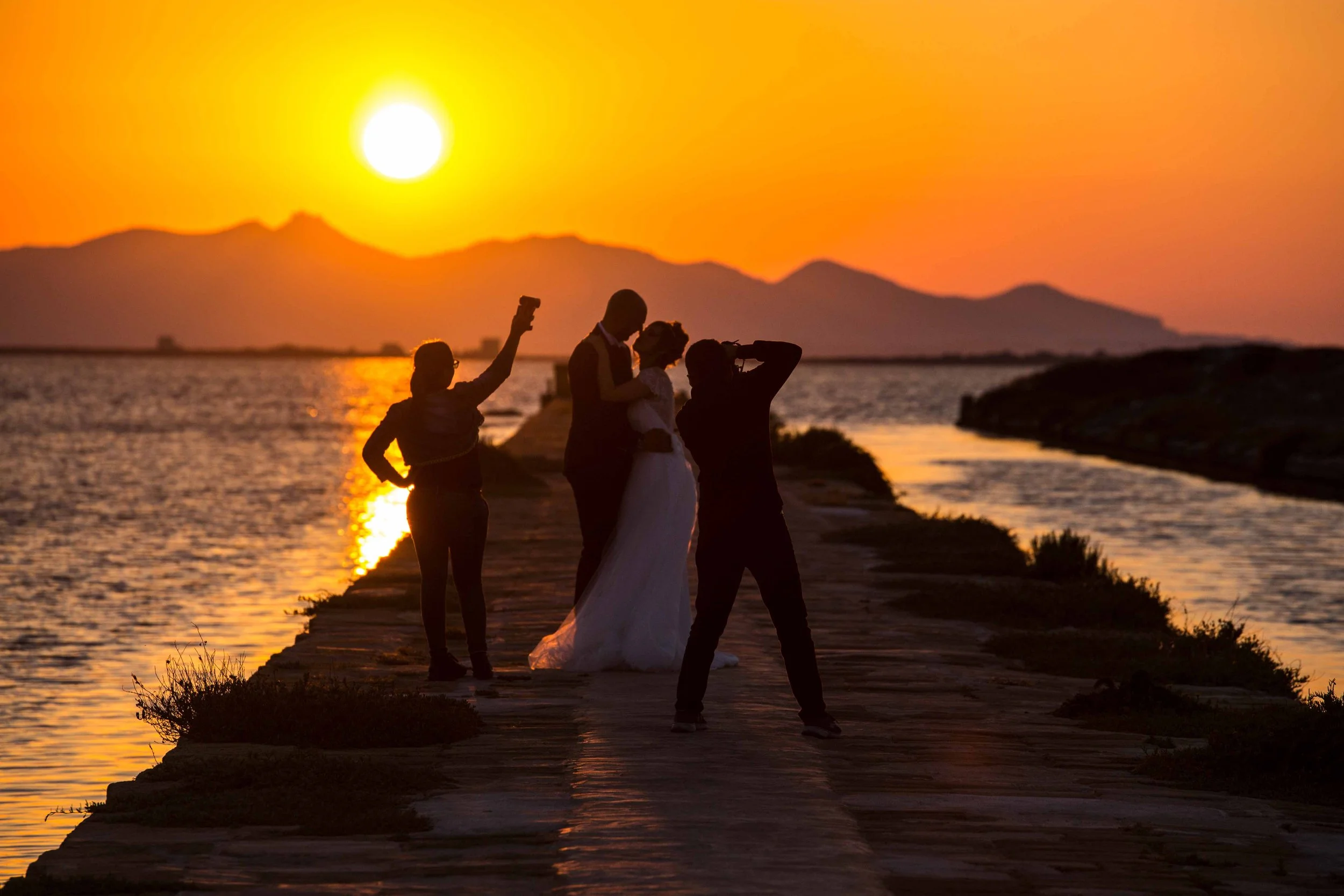 Sicily salt flats wedding shoot at golden hour — figures in silhouette on stone pier — fine art street photography print by Hermes Gray, limited edition
