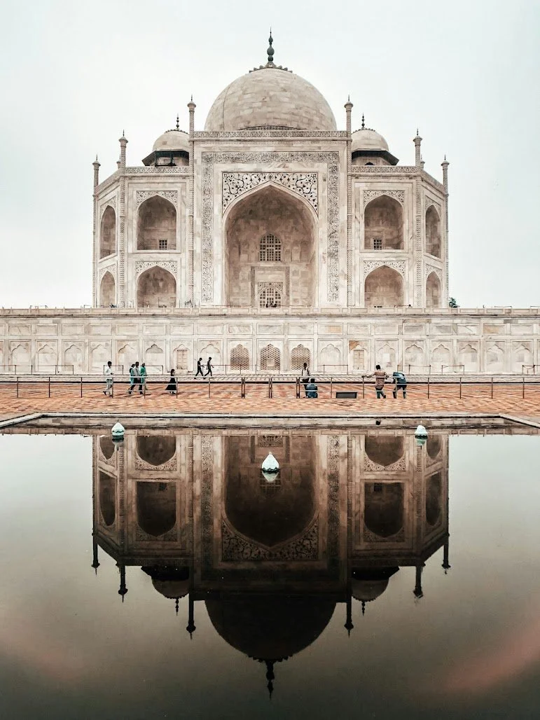 The Taj Mahal reflected in a water pool with a clear sky background.