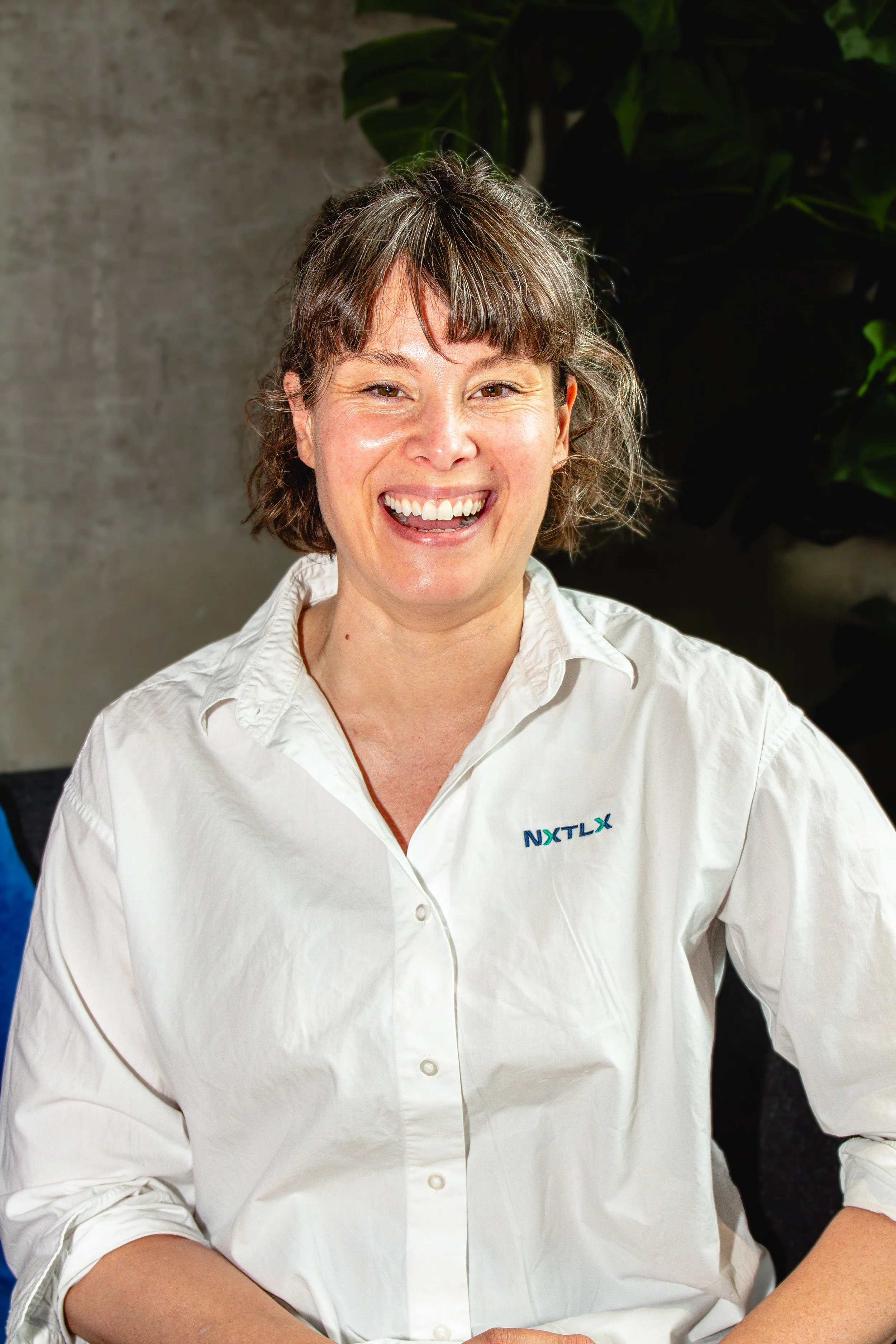 A woman with shoulder-length brown hair, wearing a light blue blazer and a beige T-shirt, is reading a document at an indoor event. She has a name tag and is focused on the paper she is holding.