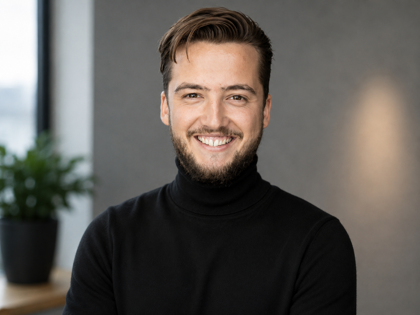 Simon Bail Startup Advisor and Founder with a beard smiling, wearing a black turtleneck, indoors with a blurred background and a potted plant.