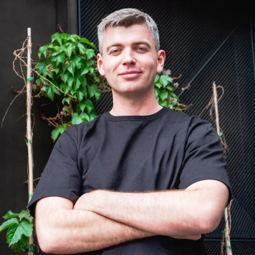 A young man with a black shirt and plants in backround
