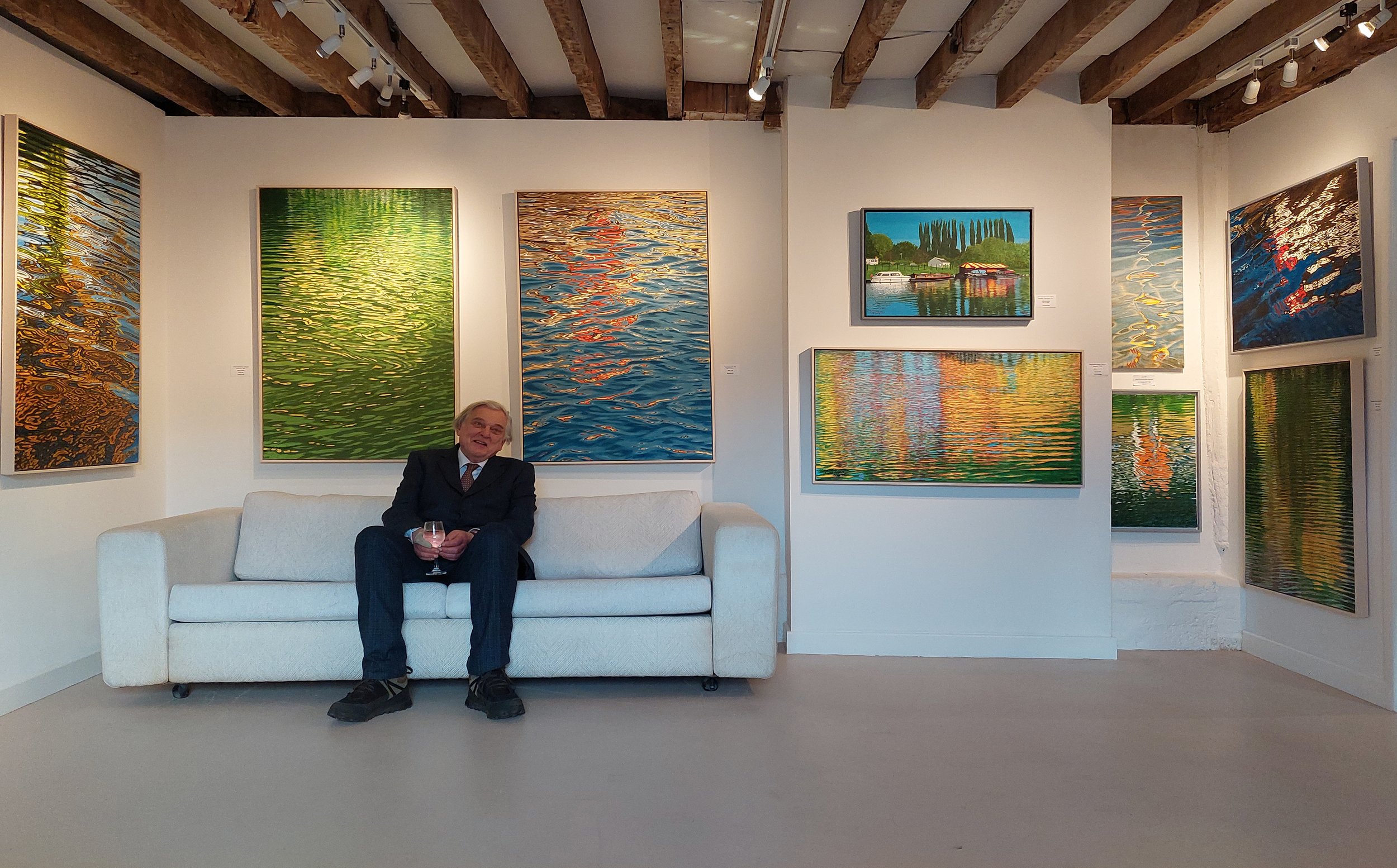 Artist Bill Pike sitting in front of his art work and paintings