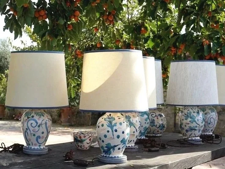 Several ceramic table lamps with white shades and blue floral patterns sitting on a wooden surface outdoors, with a fruit tree and green leaves in the background.