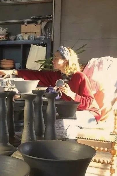 Woman sitting on a couch with a headscarf, reaching for dishes on a table in a rustic kitchen setting.
