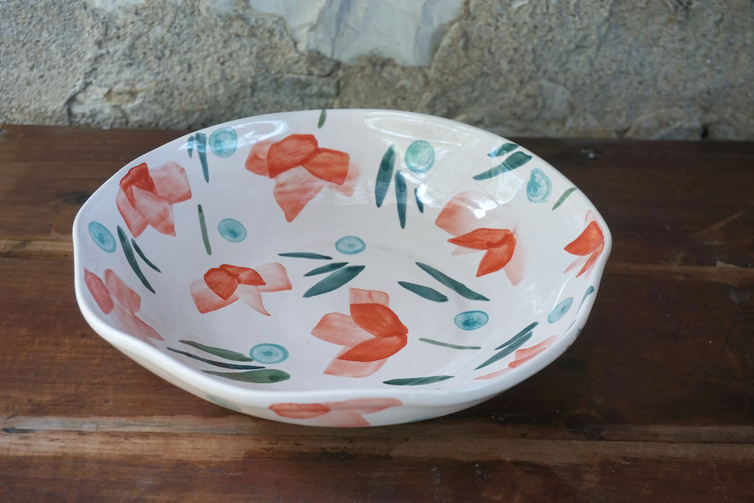 Decorative ceramic bowl with orange and blue floral patterns, placed on a wooden surface against a stone wall background.
