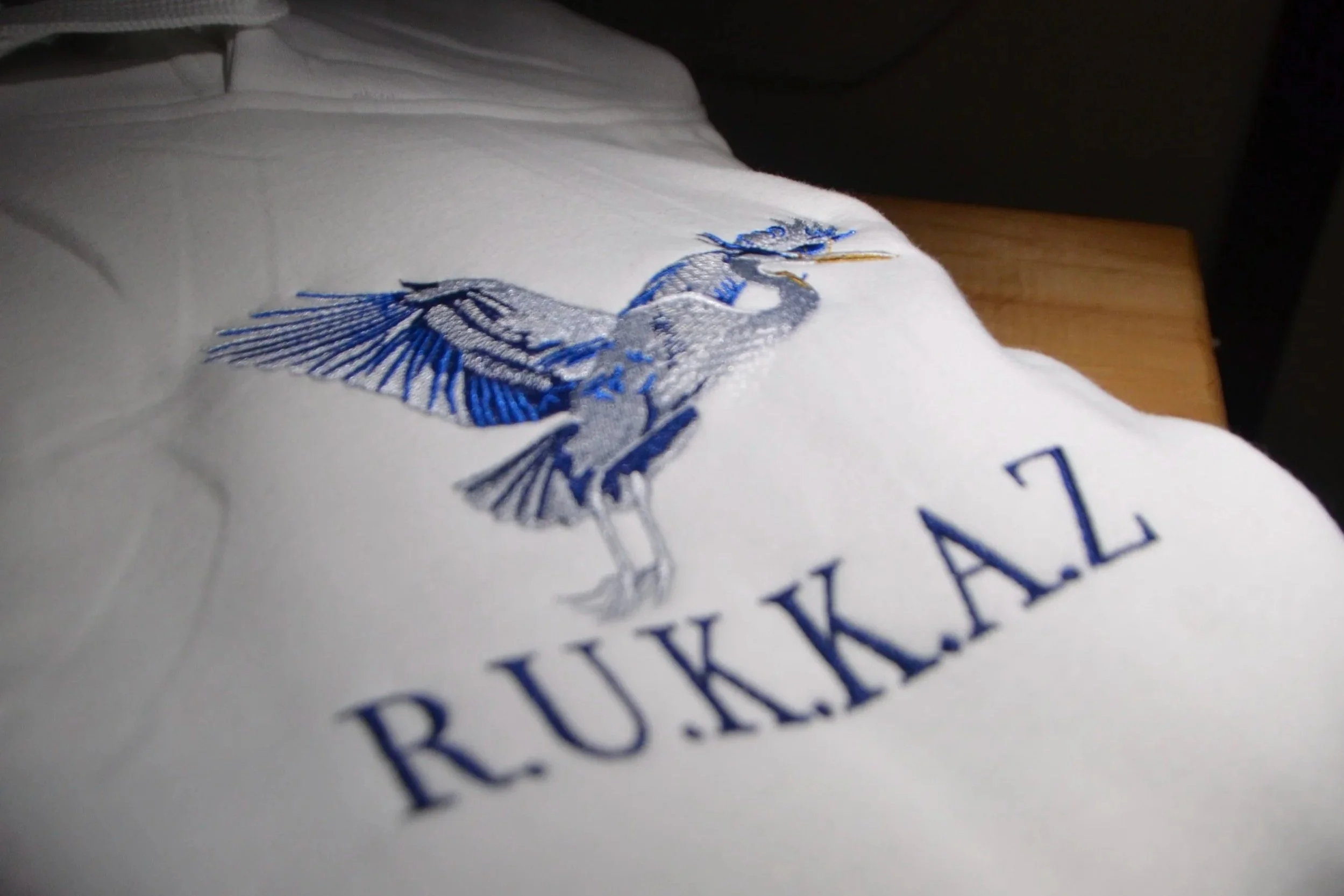 Close-up of embroidered logo featuring a great blue heron on white fabric, a part of clothing or merchandise.