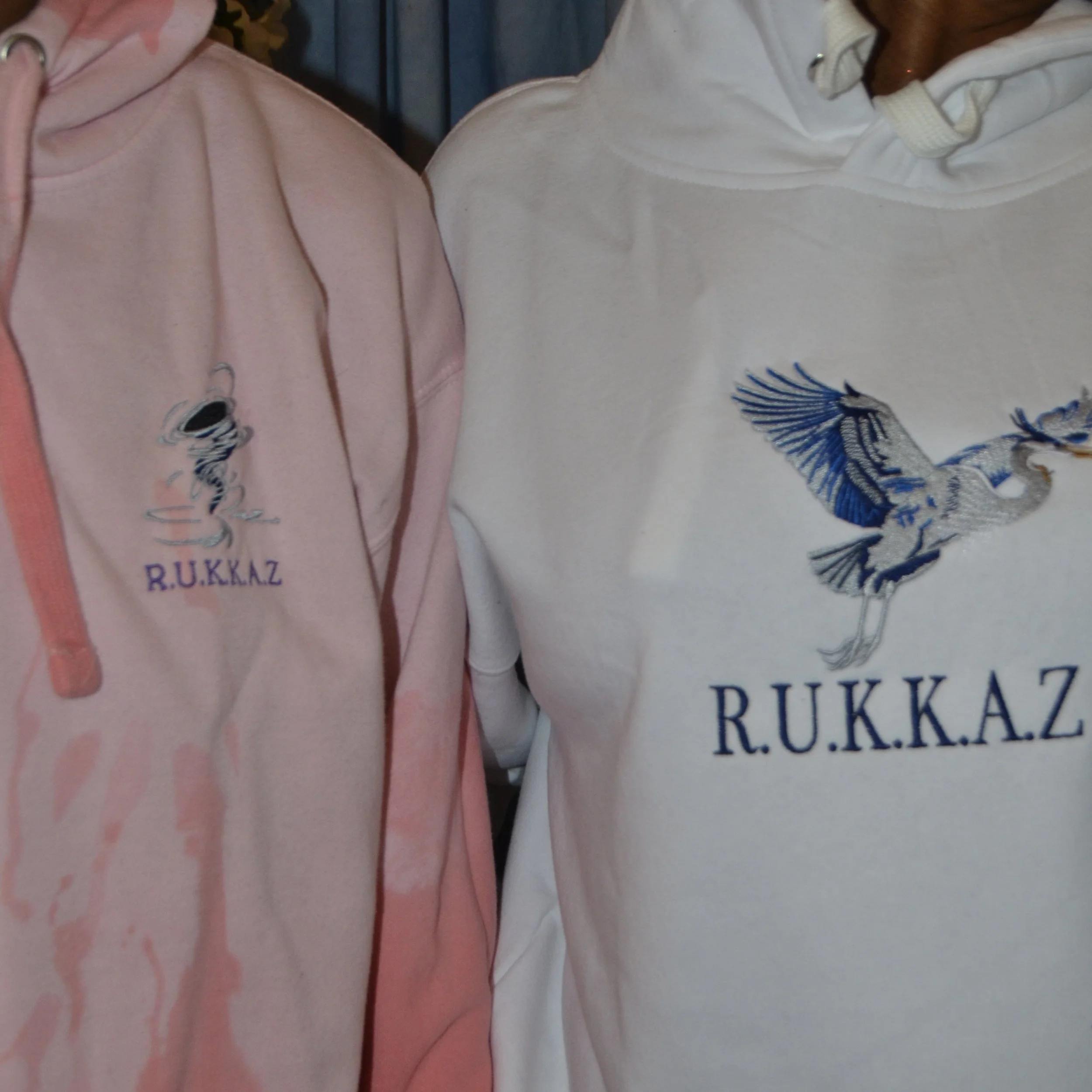 Close-up of two people wearing embroidered clothing, one in pink and the other in white, with visible embroidery and text on the fabric.