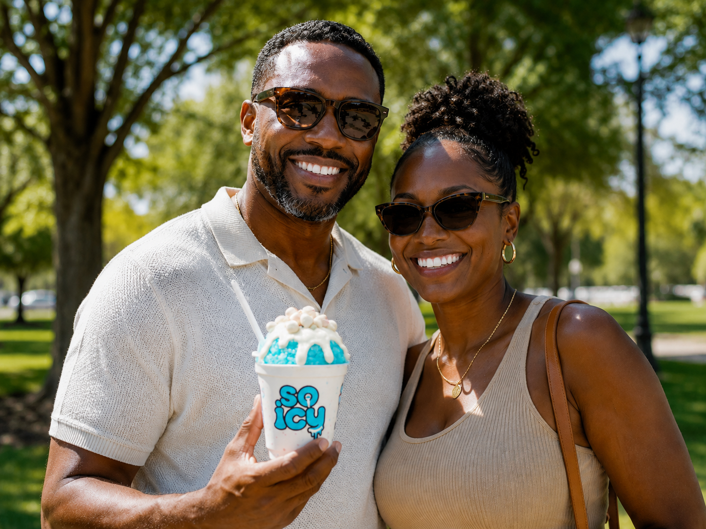 Smiling couple with sunglasses outdoors, holding a blue and white ice cream cup labeled 'SO ICY,' surrounded by trees and sunlight.