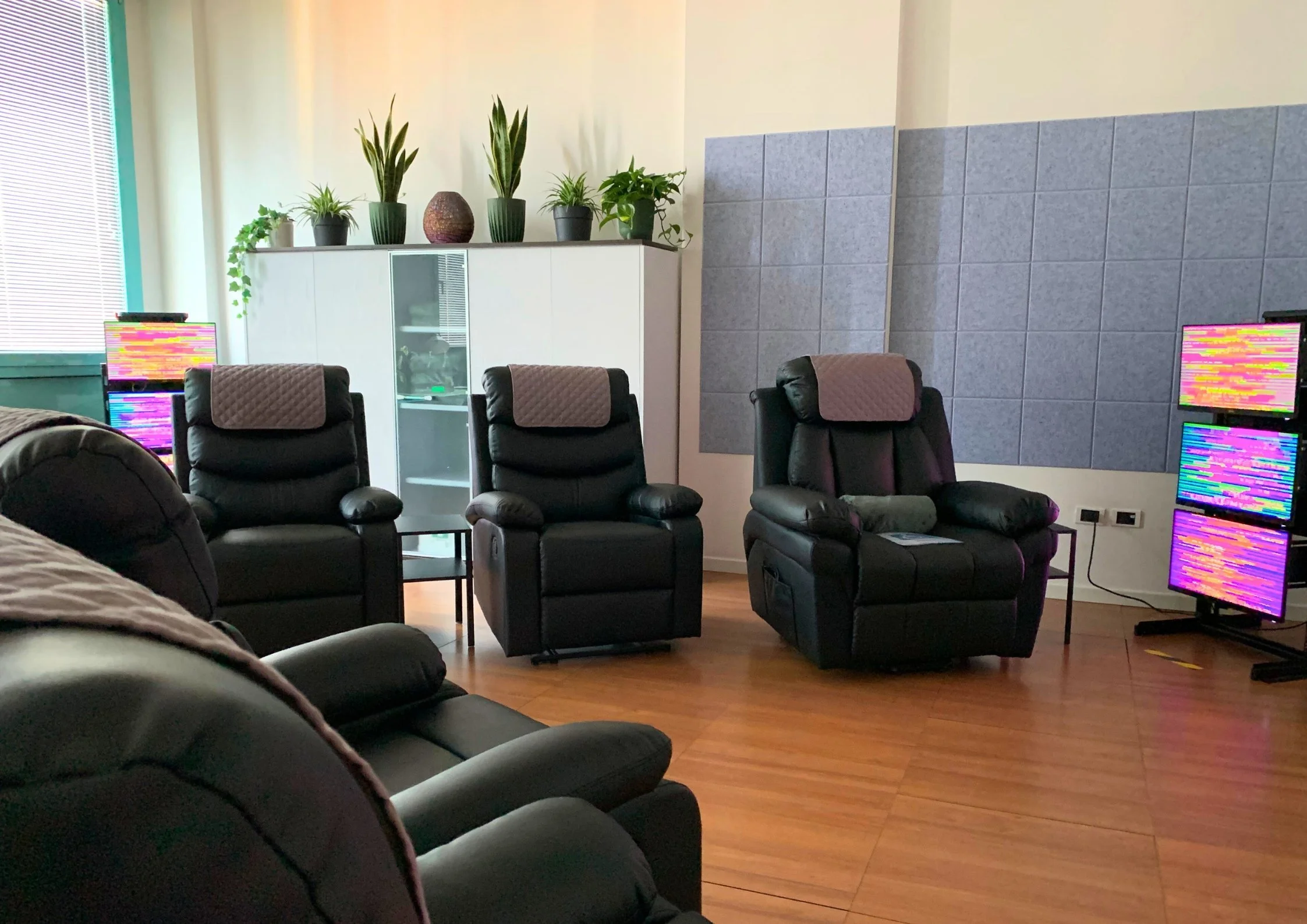 Sala centro olistico con poltrone nere, piante in vaso sul mobile bianco, pareti rivestite con pannelli isolanti, tecnologia EESystem Light System nei quattro angoli della stanza creando un campo elettromagnetico.