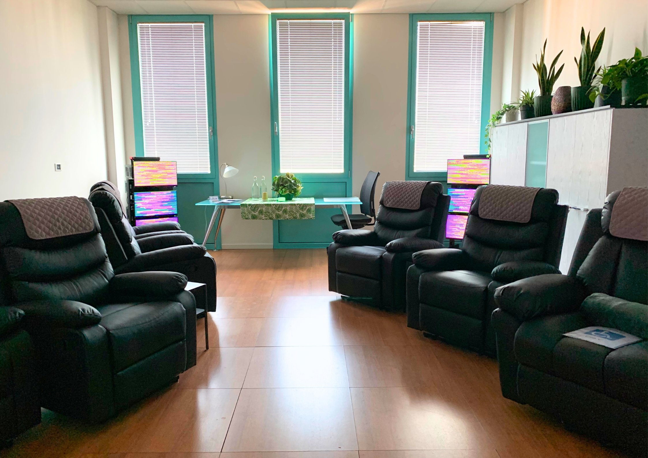 Sala centro olistico con poltrone nere, piante in vaso sul mobile bianco, pareti rivestite con pannelli isolanti, tecnologia EESystem Light System nei quattro angoli della stanza creando un campo elettromagnetico.