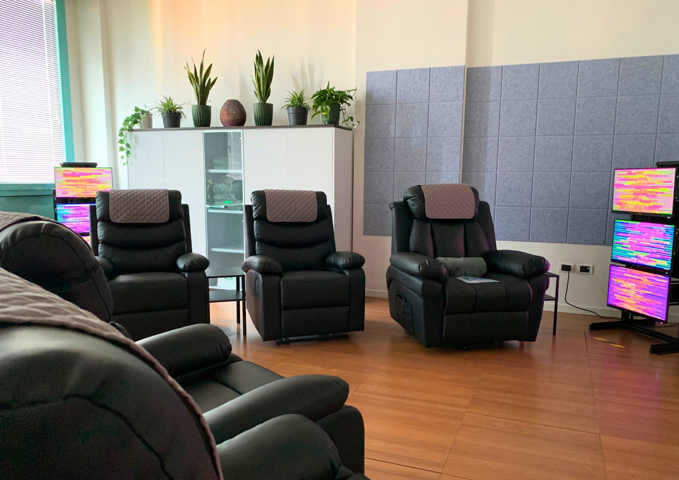 Sala centro olistico con poltrone nere, piante in vaso sul mobile bianco, pareti rivestite con pannelli isolanti, tecnologia EESystem Light System nei quattro angoli della stanza creando un campo elettromagnetico.