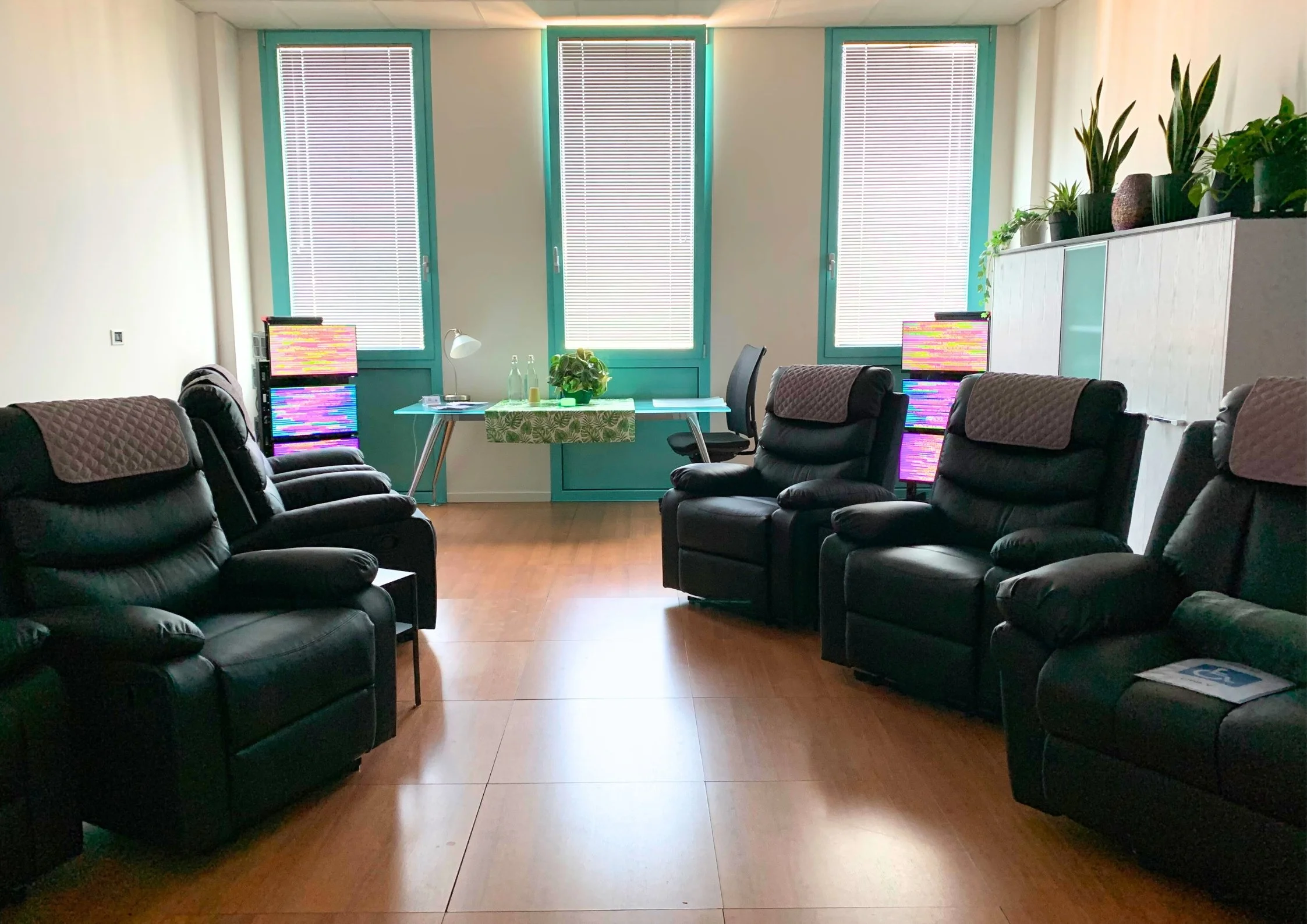 Sala centro olistico con poltrone nere, piante in vaso sul mobile bianco, pareti rivestite con pannelli isolanti, tecnologia EESystem Light System nei quattro angoli della stanza creando un campo elettromagnetico.