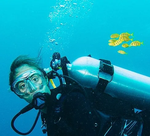Sarah Conway underwater next to a small school of yellow fish with black stripes.