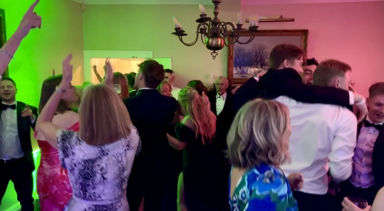 People dancing and socializing at a party with colorful lighting and a chandelier in the room.