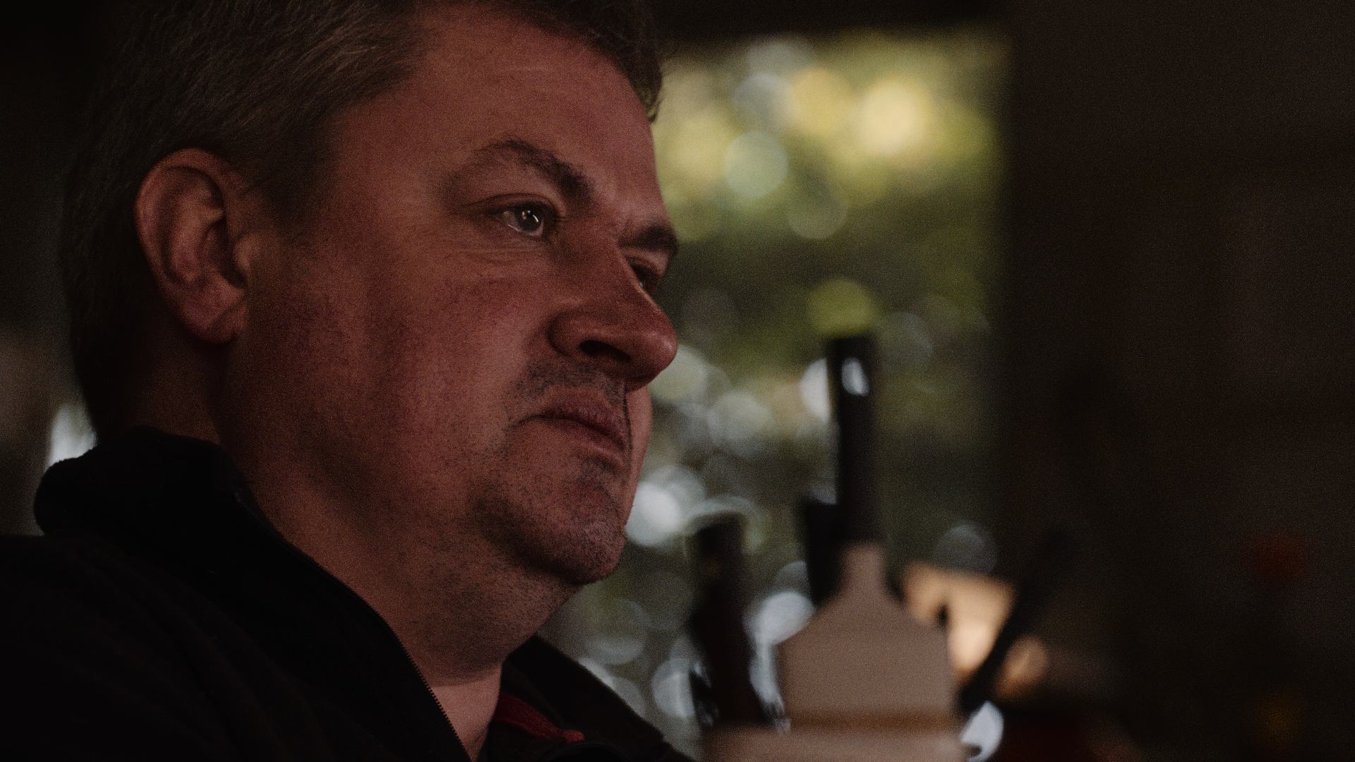 Close-up of a man's face, with a serious expression, in profile view. Blurred background with bokeh effect.