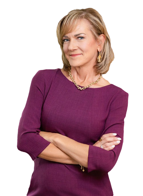 A confident middle-aged woman with blonde hair, wearing a purple dress with three-quarter sleeves, gold jewelry including hoop earrings, a necklace, and rings, standing with arms crossed and smiling.