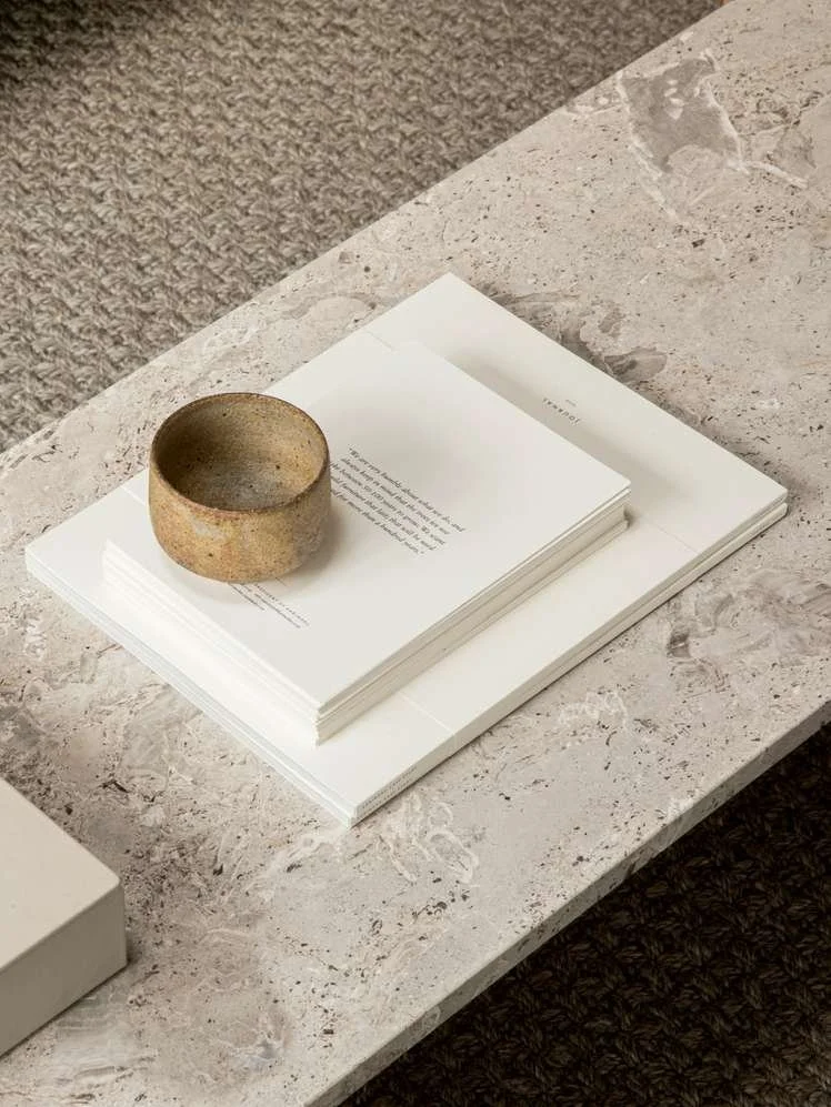 A stone or ceramic bowl placed on a white book, which is on top of a larger white notebook or sketchpad on a gray marble surface.