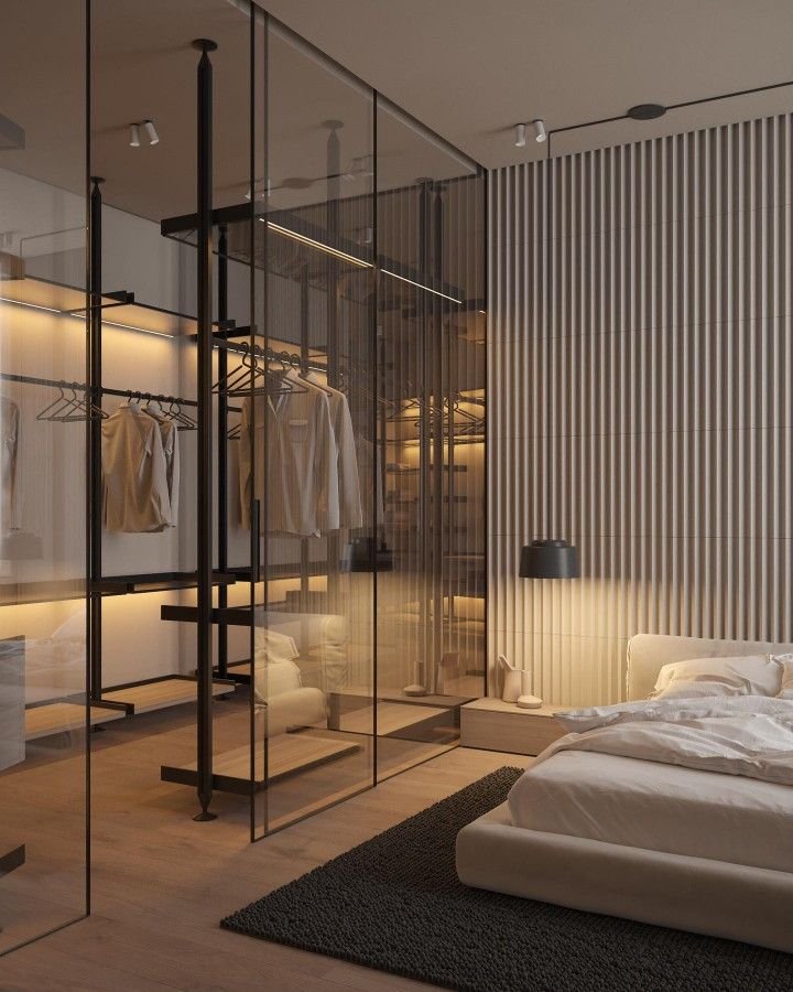 Modern bedroom with a glass partition closet containing hanging clothes and open shelves, a low bed with white bedding, a black wall-mounted lamp, and a textured wall panel.