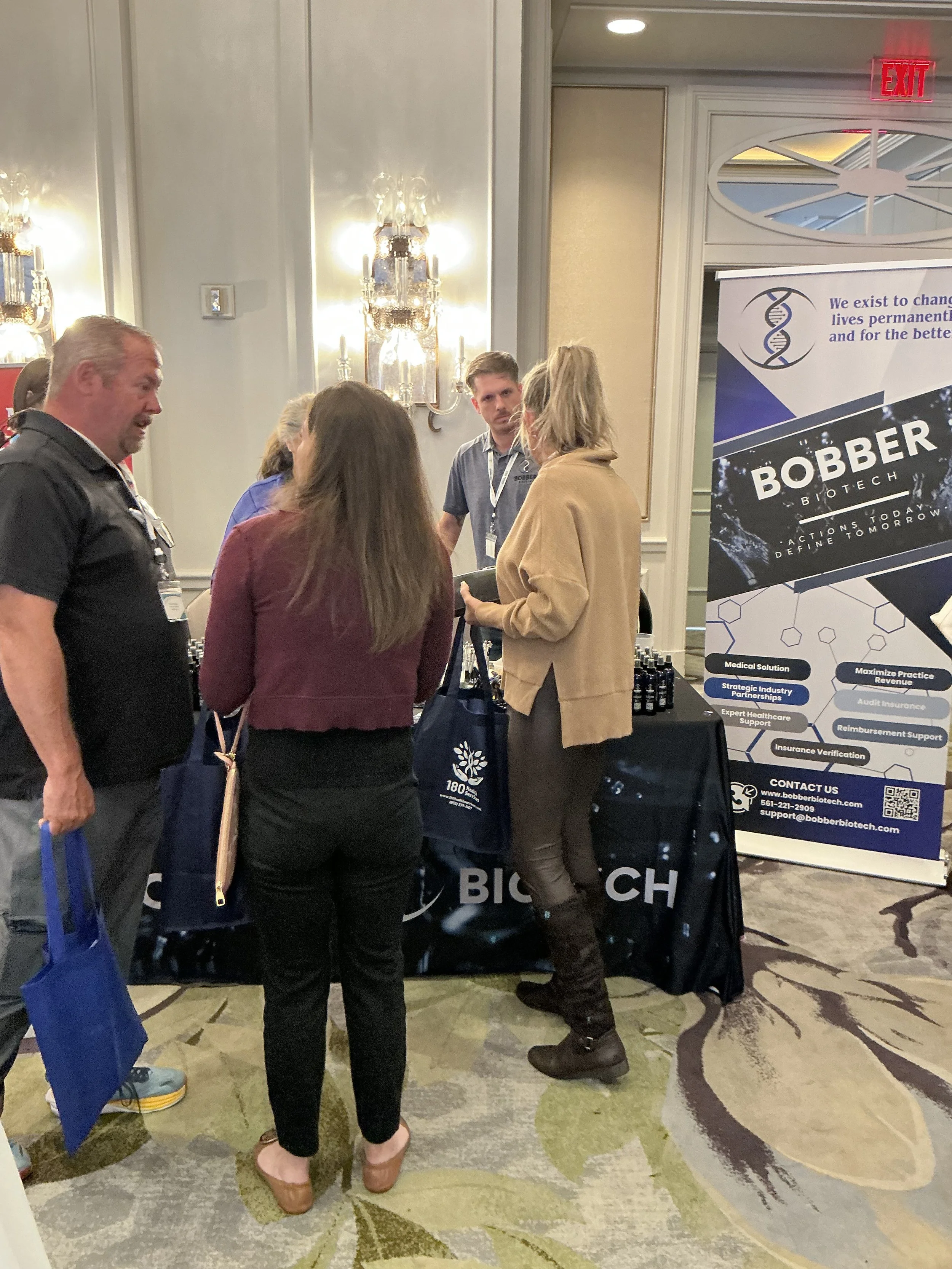 Group of people at a conference or trade show booth related to biotech. There are four individuals engaged in conversation, with a table displaying products, and a banner with information about Bobber Biotech.