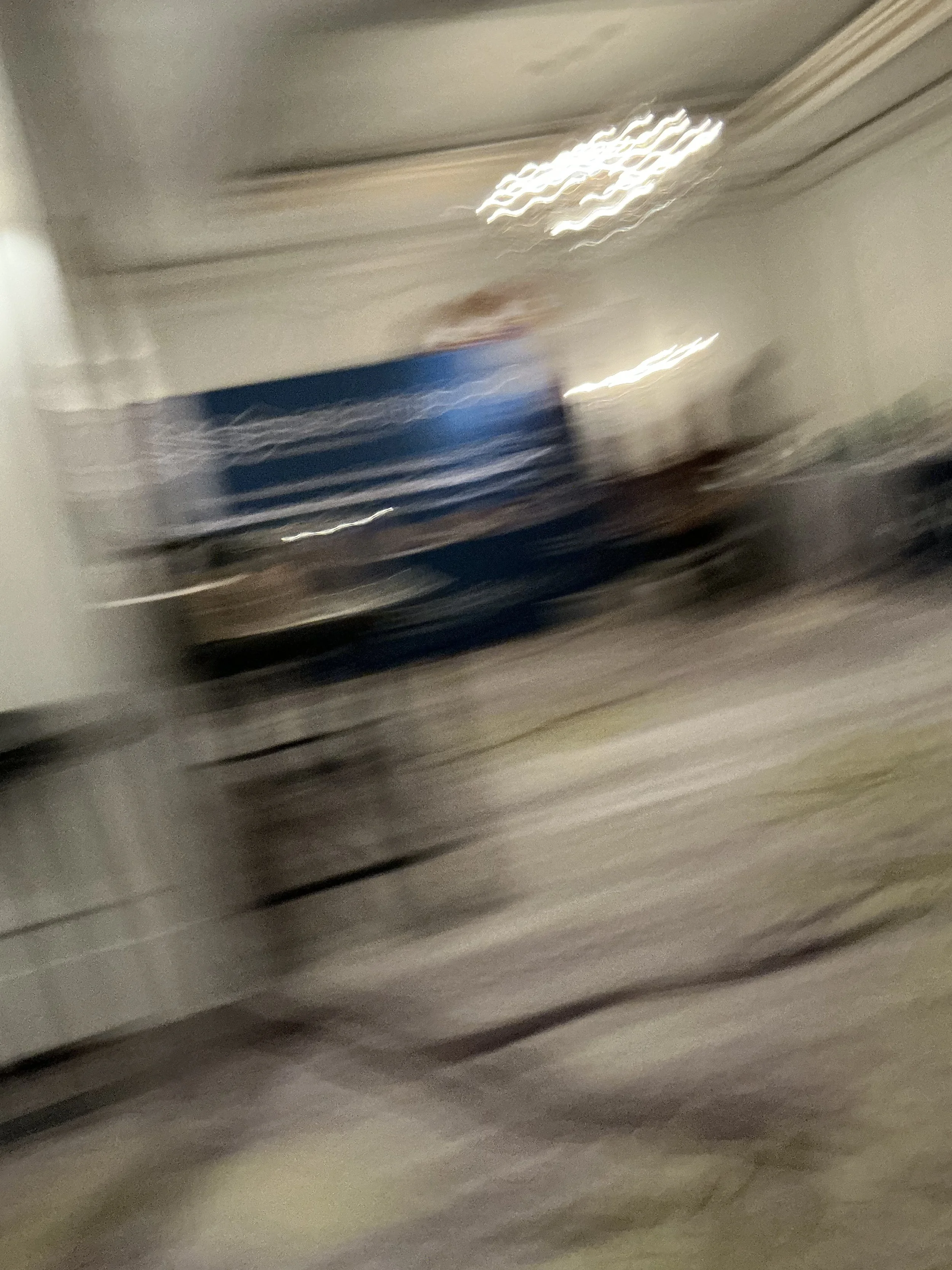 Blurry photo of a room with a person in a blue shirt standing near some furniture and a wall with lights.