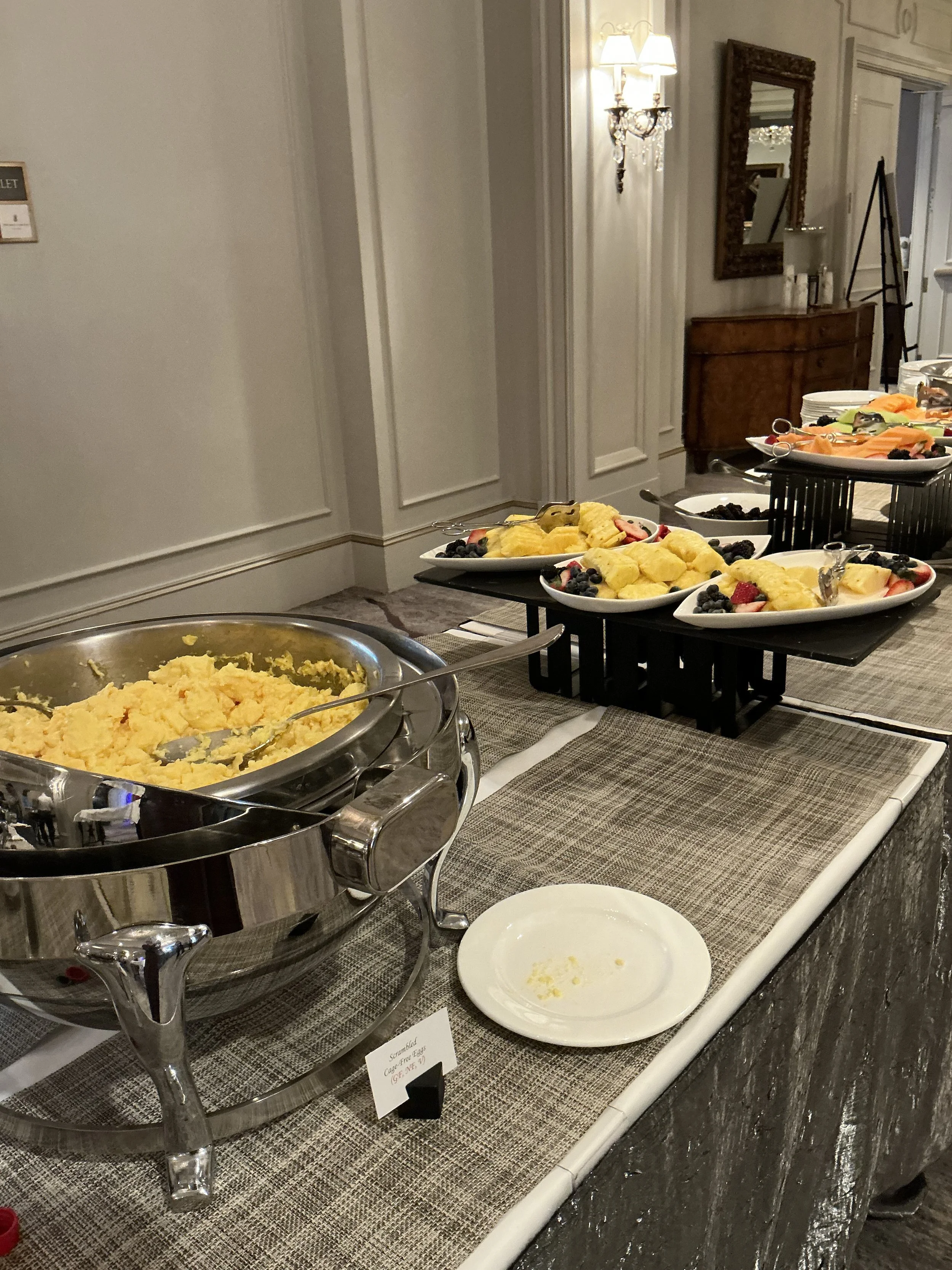 Buffet table with scrambled eggs, fruit, and other breakfast foods at a hotel or restaurant.