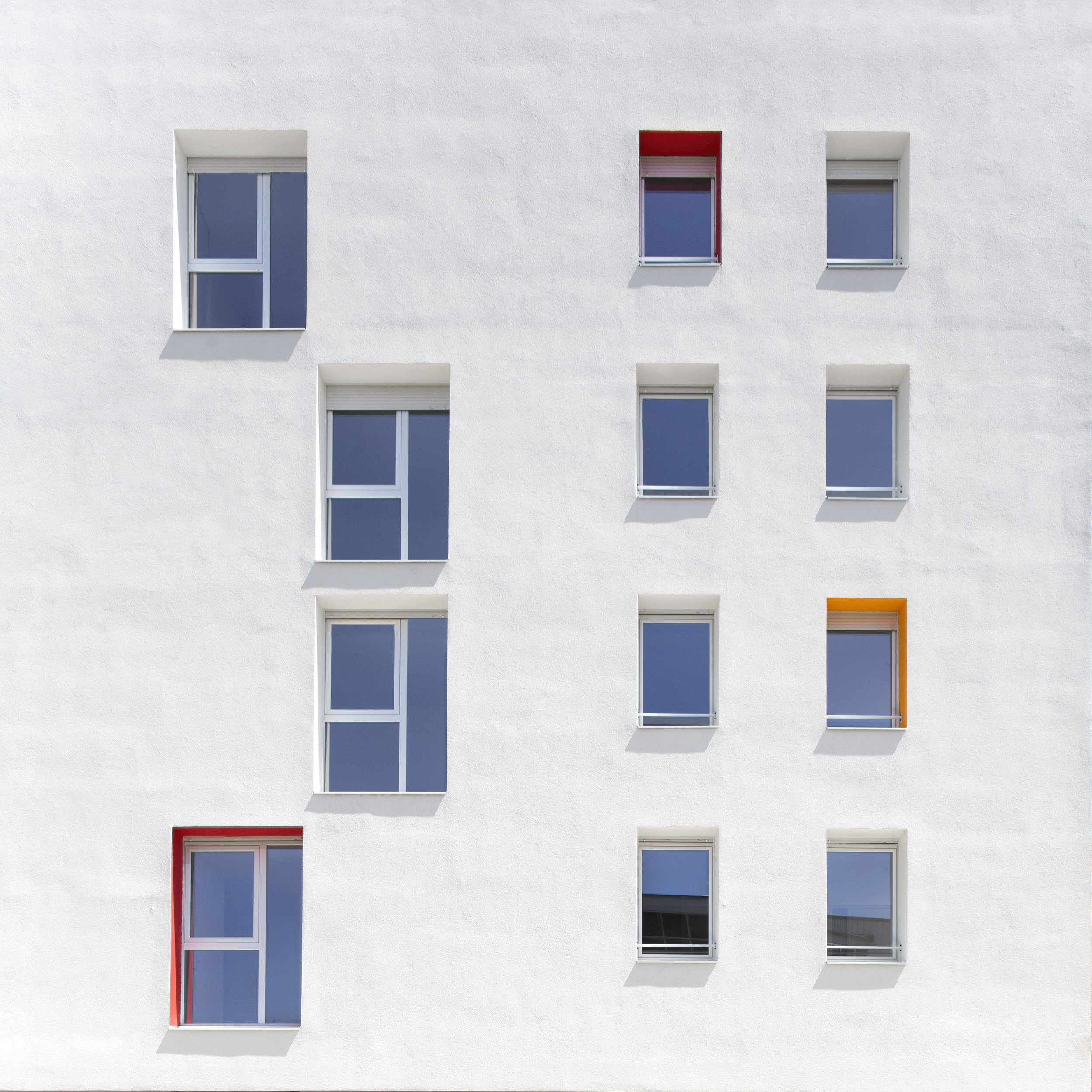 Façade d'un immeuble blanc avec plusieurs fenêtres, dont une avec un cadre rouge et une avec un cadre orange.