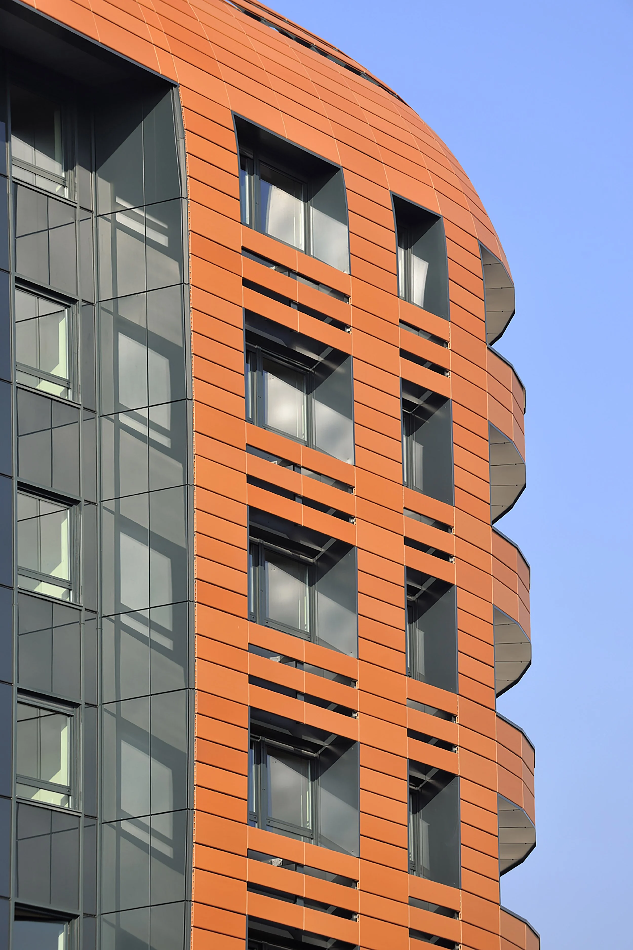 Bâtiment moderne avec façade orange et fenêtres en verre, sous un ciel bleu clair.