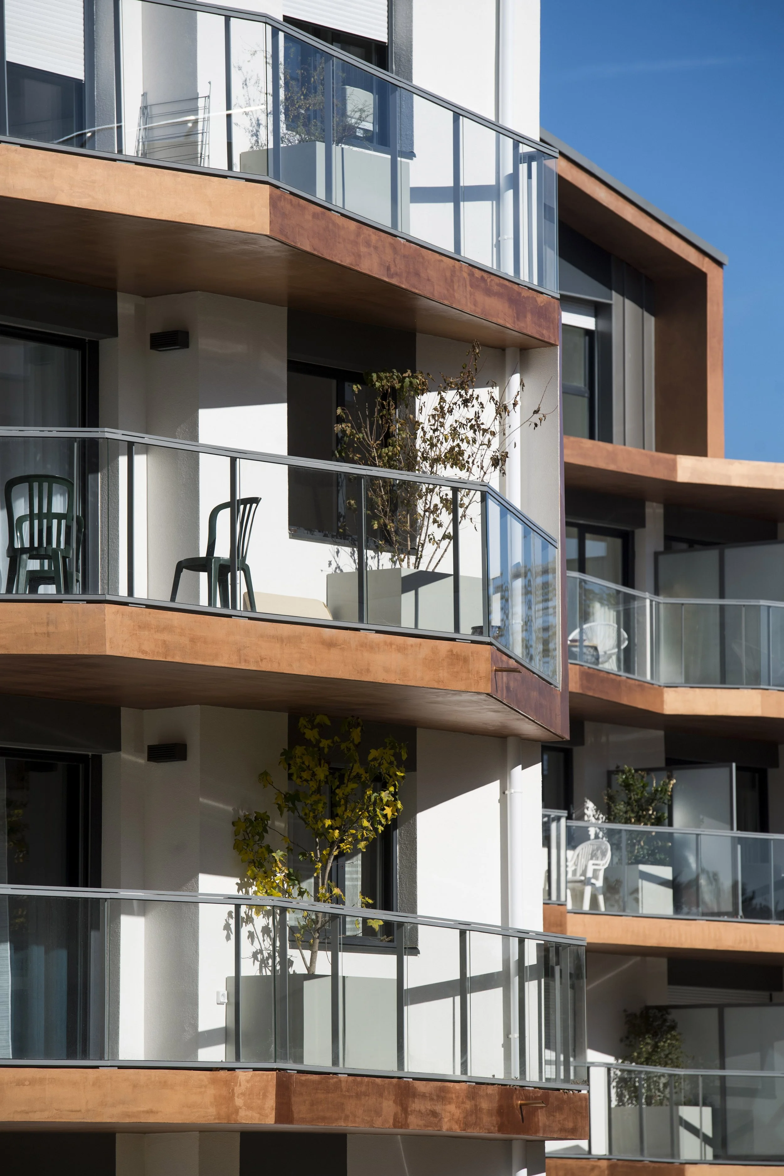 Un immeuble résidentiel moderne avec plusieurs balcons, en partie entourés de rampes en verre, sous un ciel clair.