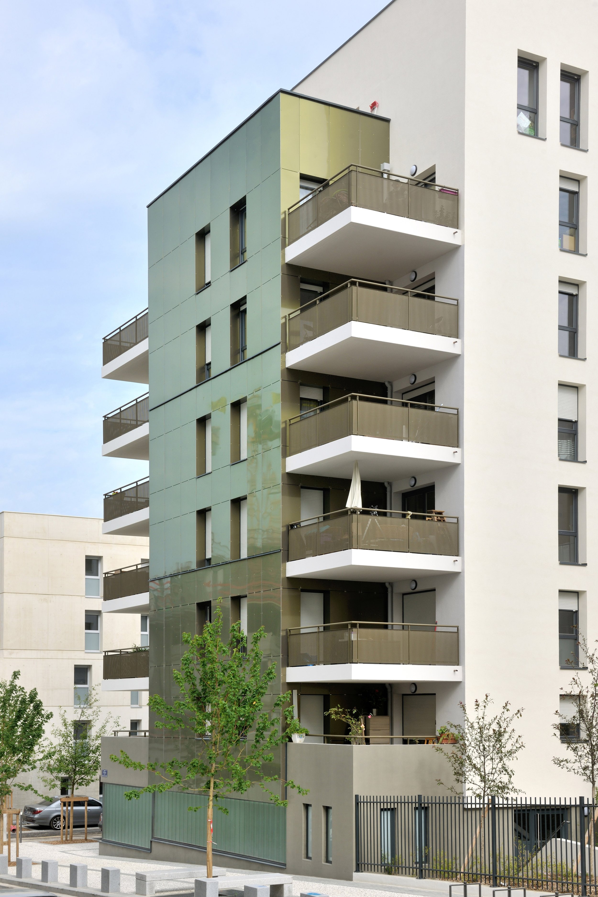 Faculté de bâtiment moderne avec plusieurs balcons en béton, fenêtres rectangulaires, et façade en parpaings clairs et en panneaux métalliques vert grisâtre.