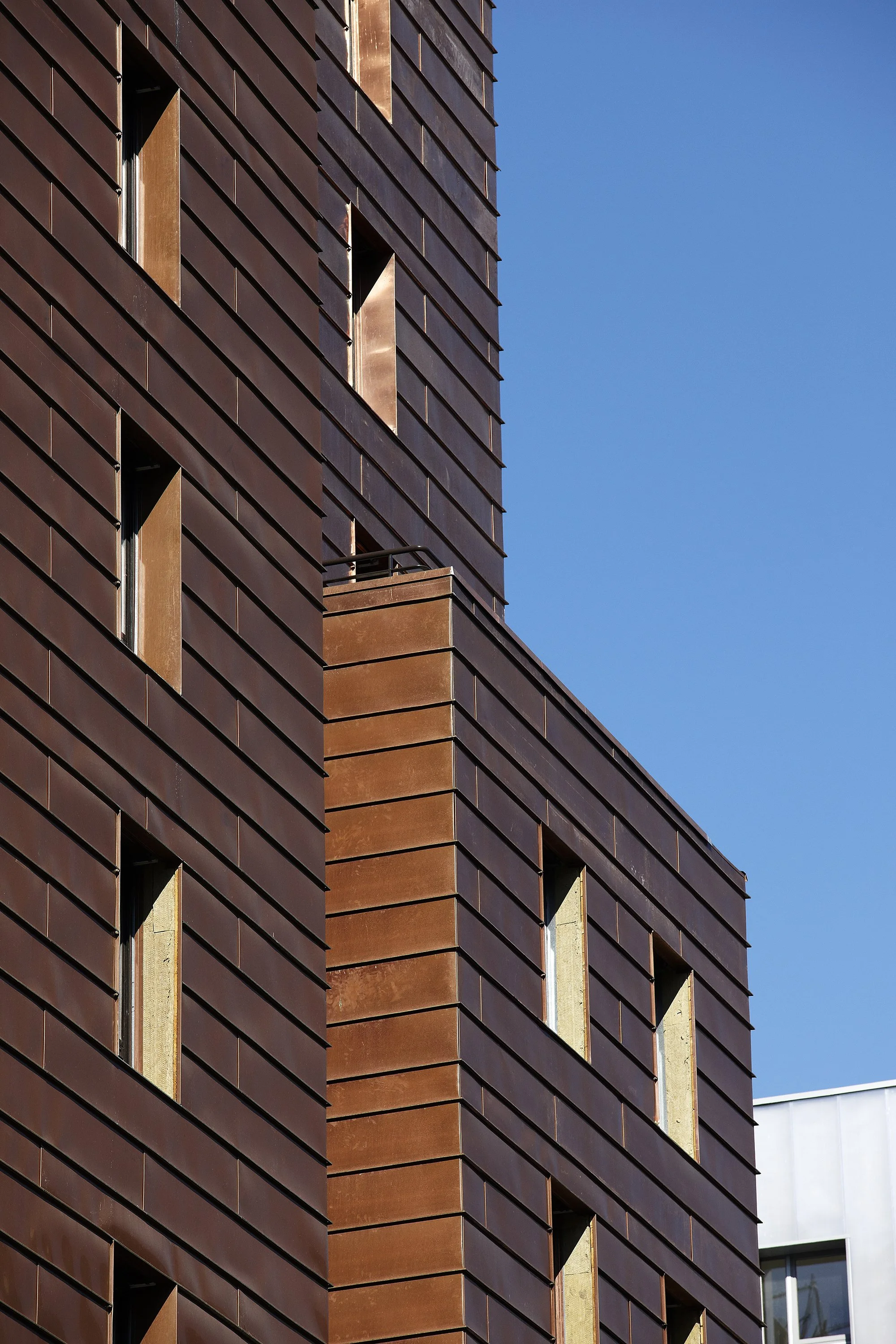 Un bâtiment moderne avec une façade en métal brossé de couleur marron, avec plusieurs fenêtres rectangulaires et un ciel bleu en arrière-plan.
