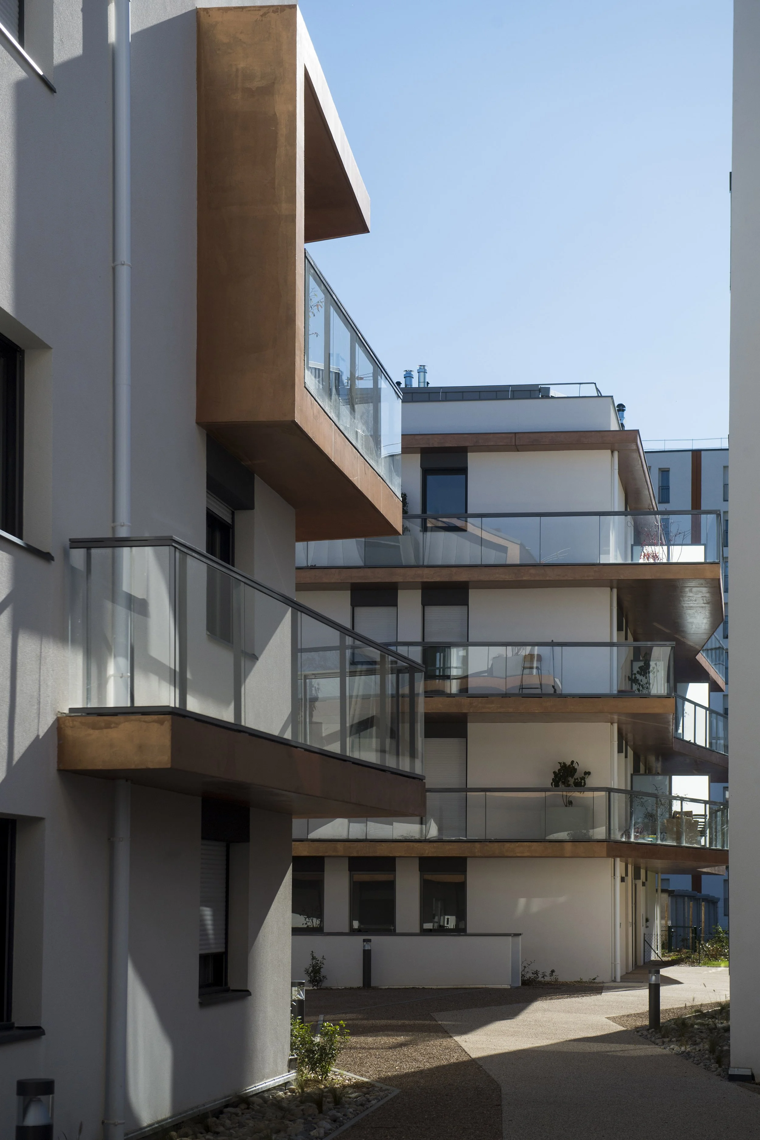 Immeuble résidentiel moderne avec balcons en verre et façades en blanc et brun, sous un ciel dégagé.