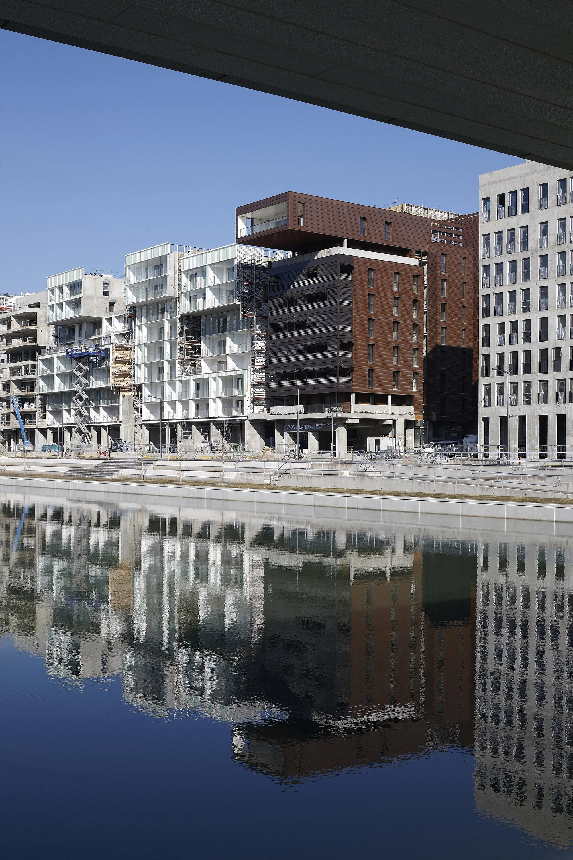 Construction de bâtiments modernes le long d'un plan d'eau avec reflection dans l'eau, ciel bleu en arrière-plan.