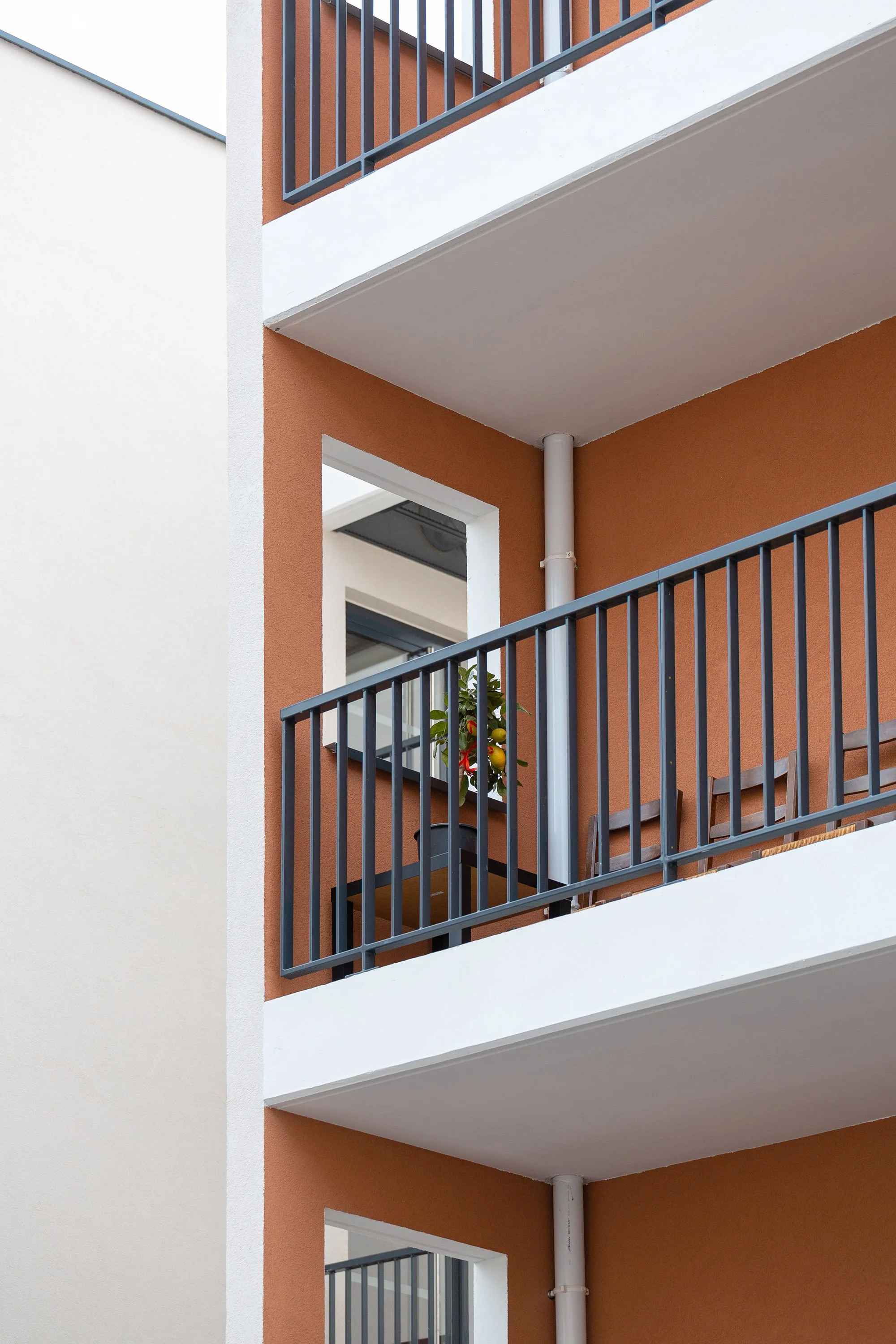Vue partielle d'un immeuble résidentiel avec des balcons à balustrades en métal noir, murs peints en blanc et orange, et un tuyau d'évacuation blanc.