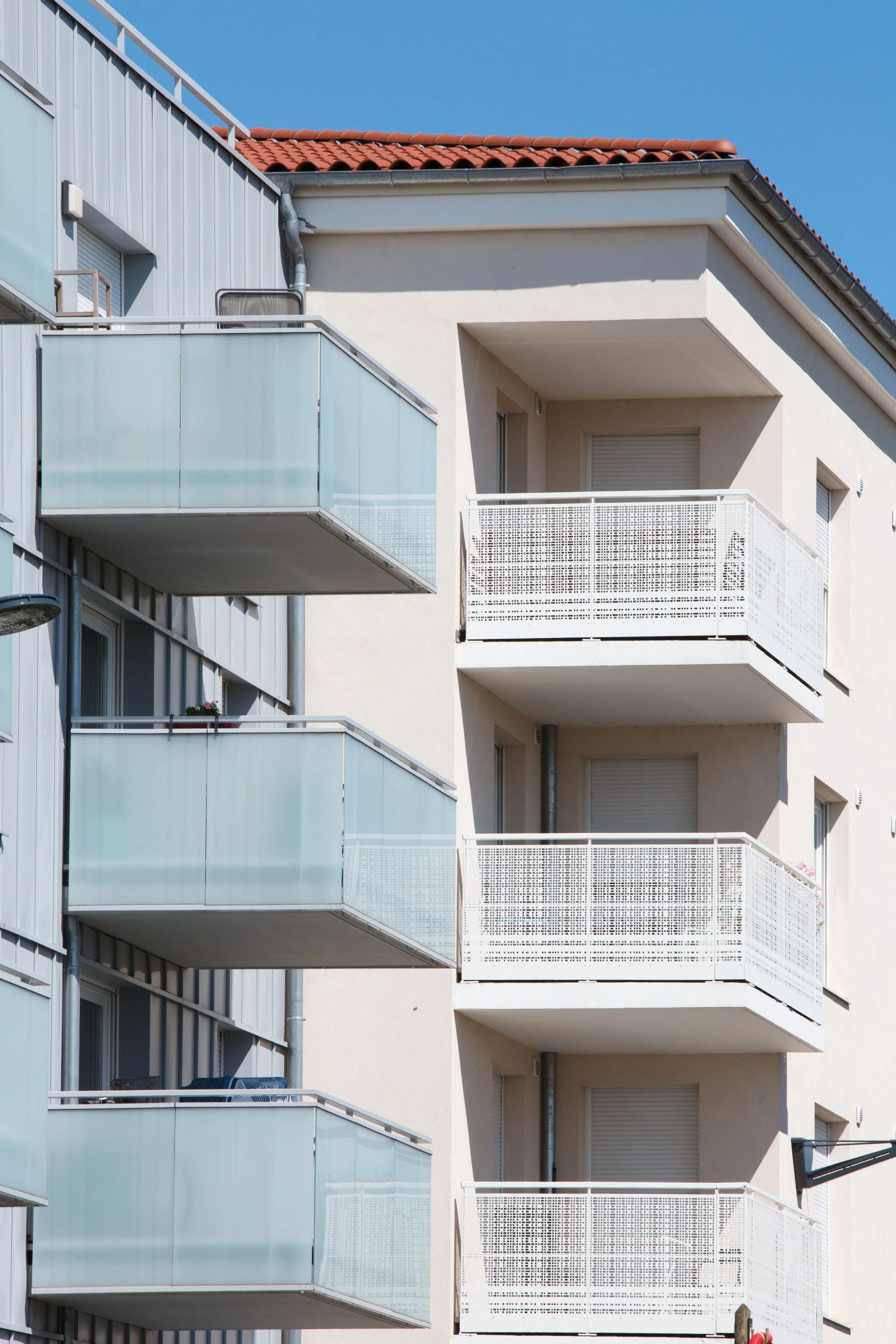 Bâtiment résidentiel avec plusieurs balcons en façade, certains avec des meubles et des décorations, sous un ciel bleu.