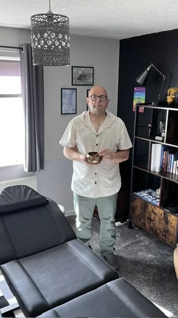 Kevin Stead, certified Angelic Reiki practitioner, holding a singing bowl in his private treatment room in South Elmsall, West Yorkshire, standing next to a comfortable black reiki couch.
