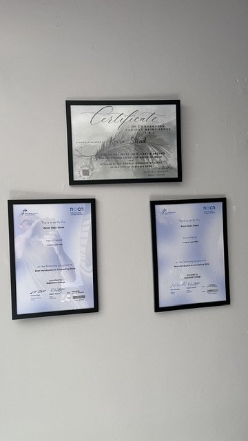 Three framed professional qualifications hanging on a wall, including Kevin Stead's Certificate of Completion for Angelic Reiki Levels 1 & 2, and two NOCN-accredited certificates for Counselling Skills.