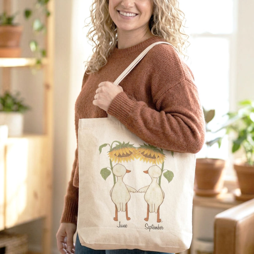 Women wearing a Cotton Tote Bag featuring hand illustrated ducks or geese with large sunflowers as umbrellas available for personalization