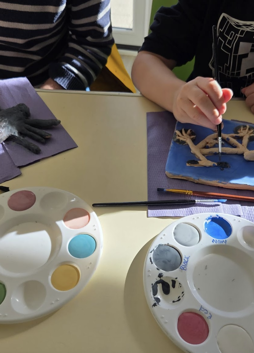 Children painting clay sculptures with paint palettes on a table.