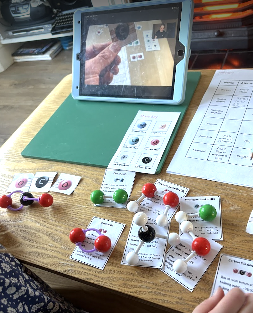 Table with chemistry models, informational cards, and a tablet showing a virtual meeting for an educational science activity.