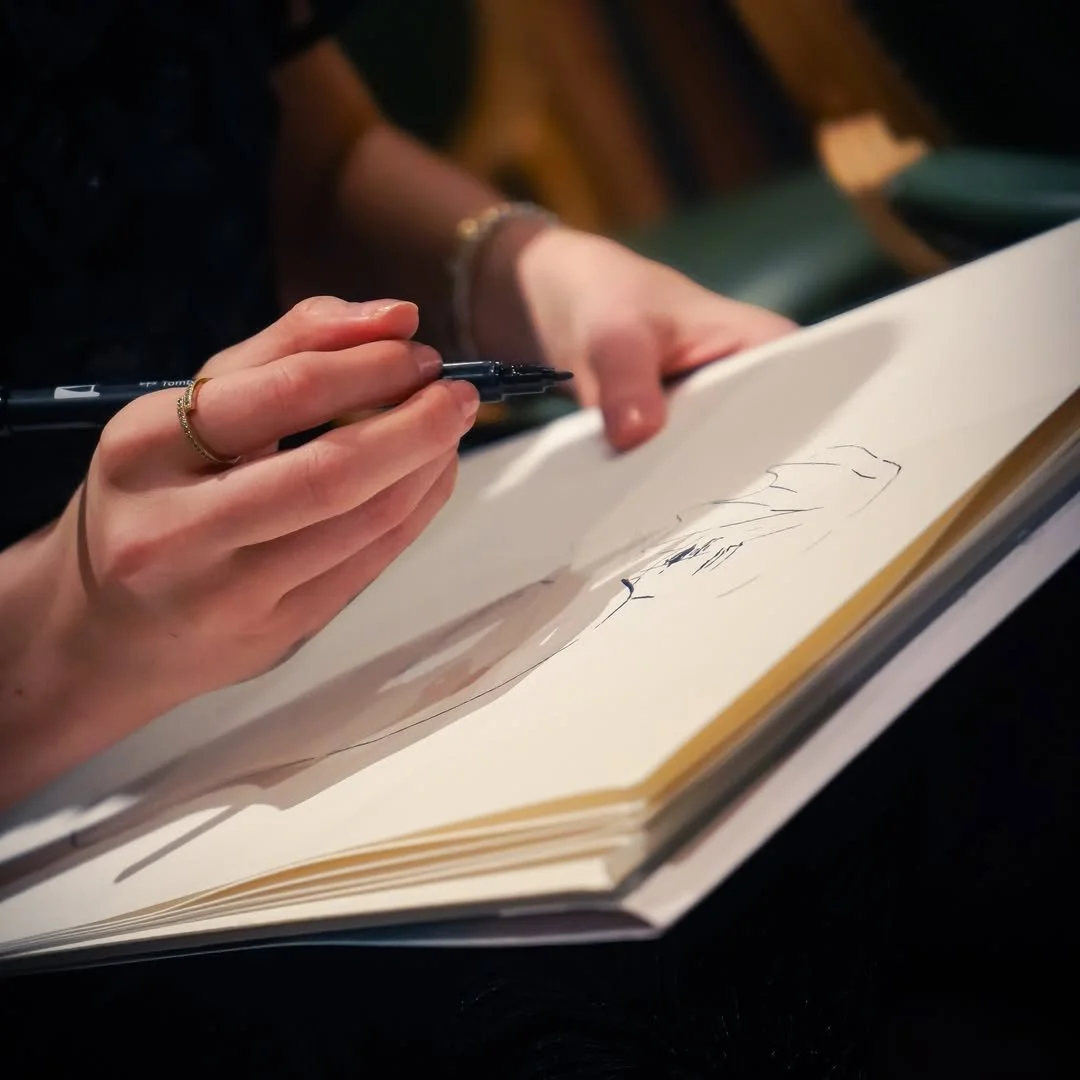 A person holding a black marker and drawing sketches or doodles in a large white sketchbook.