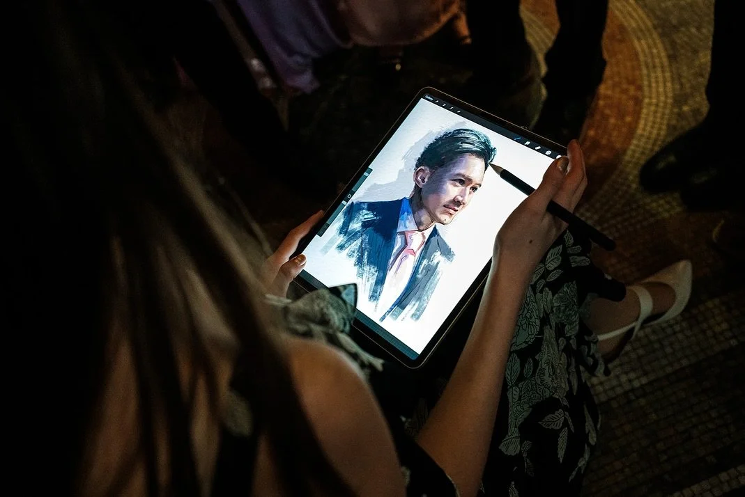 Person sketching a portrait of a man on a tablet with a stylus in a dimly lit room.