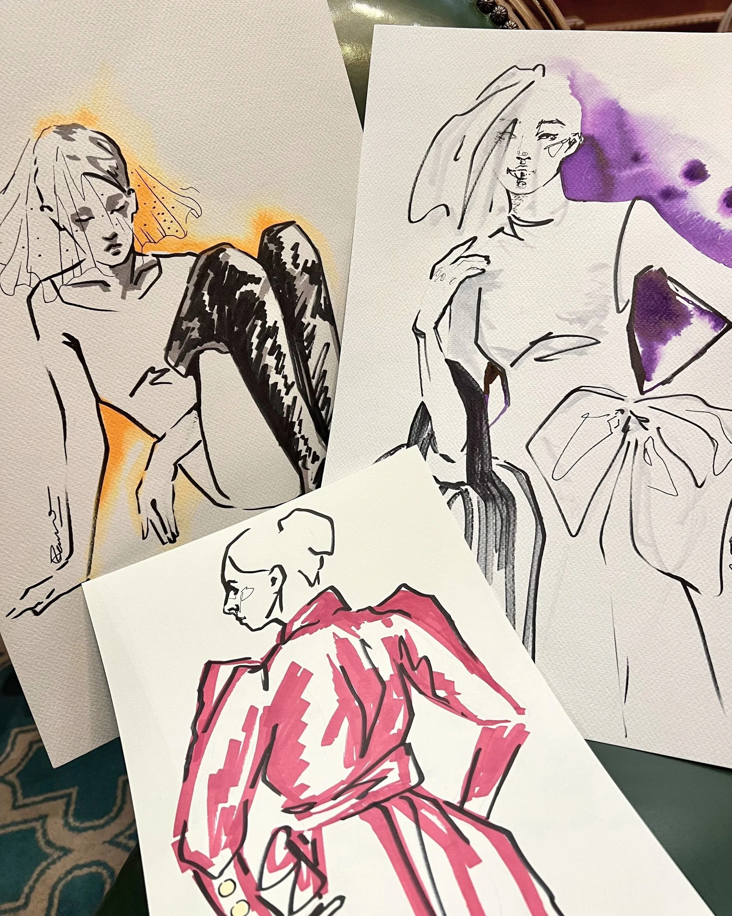 Several artistic sketches of women, some with colorful watercolor accents and others in black and white, placed on a surface.