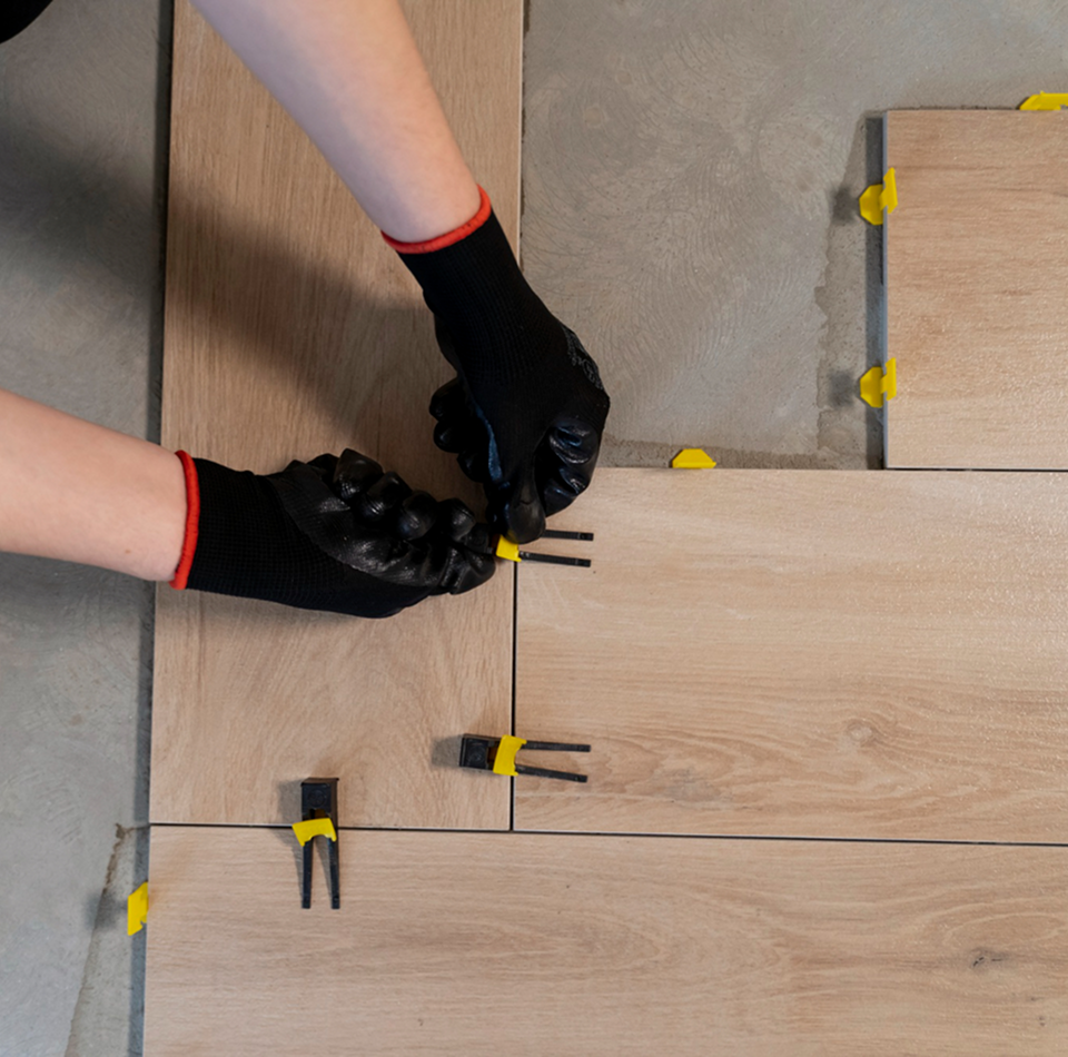 Person wearing black gloves installing wooden flooring using tile spacers.