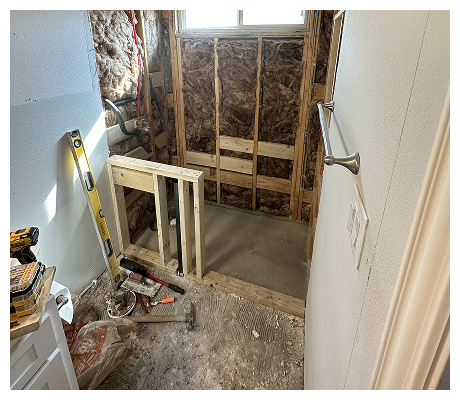 Bathroom under renovation with exposed insulation, unfinished framing, and construction tools.