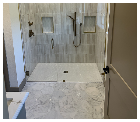 Modern walk-in shower with beige tiled walls, two built-in wall niches, a black showerhead, and marble flooring outside the shower area.