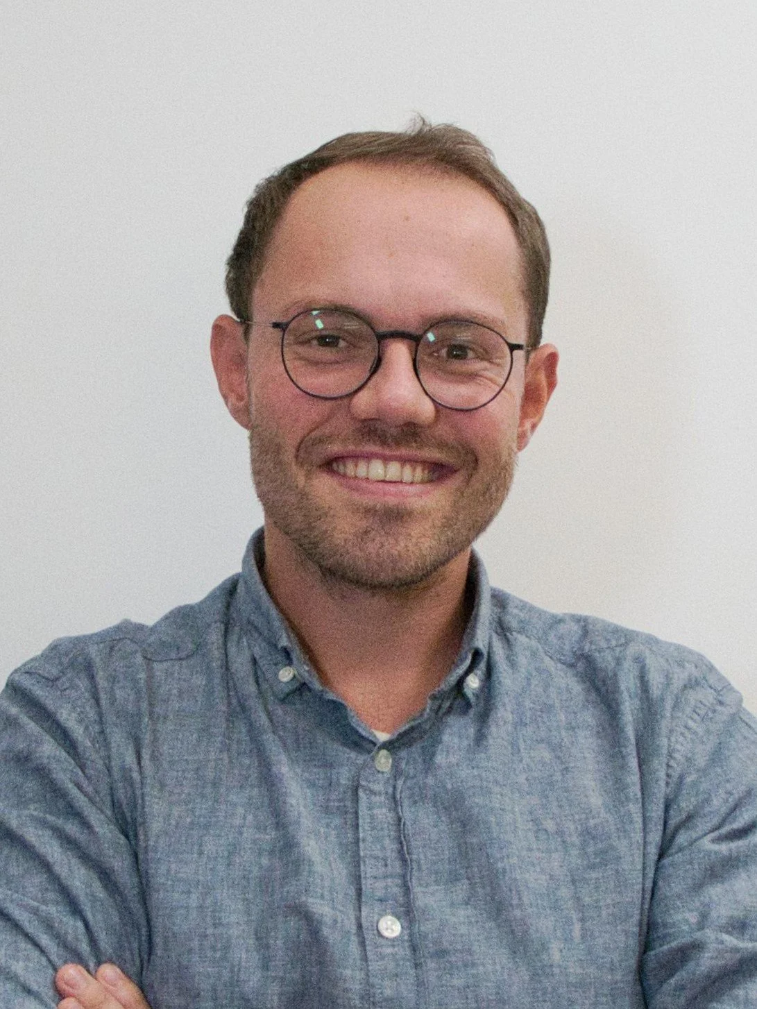 Lächelnder Mann mit Brille in Hemd vor weißem Hintergrund.