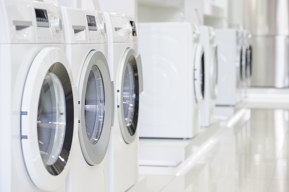 A row of white front-loading washing machines in a laundromat.