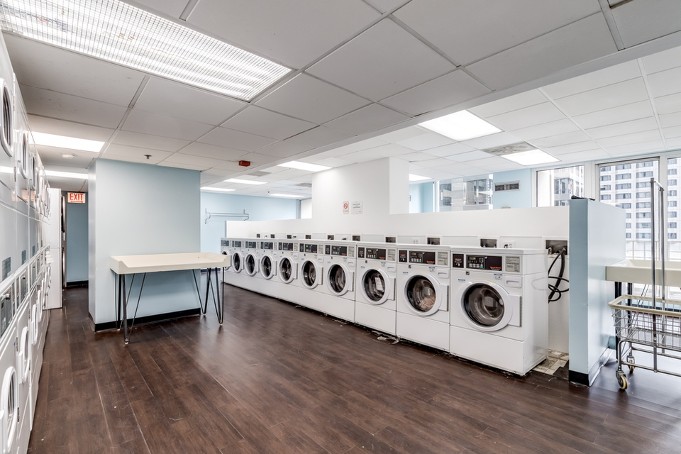 Coin-operated washing machines in a laundromat with a table and shopping cart nearby.