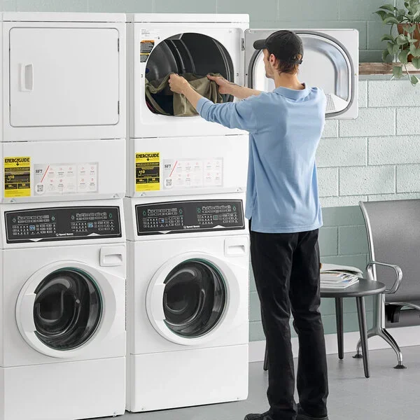 A person loading laundry into a front-loading washer and dryer in a laundromat.