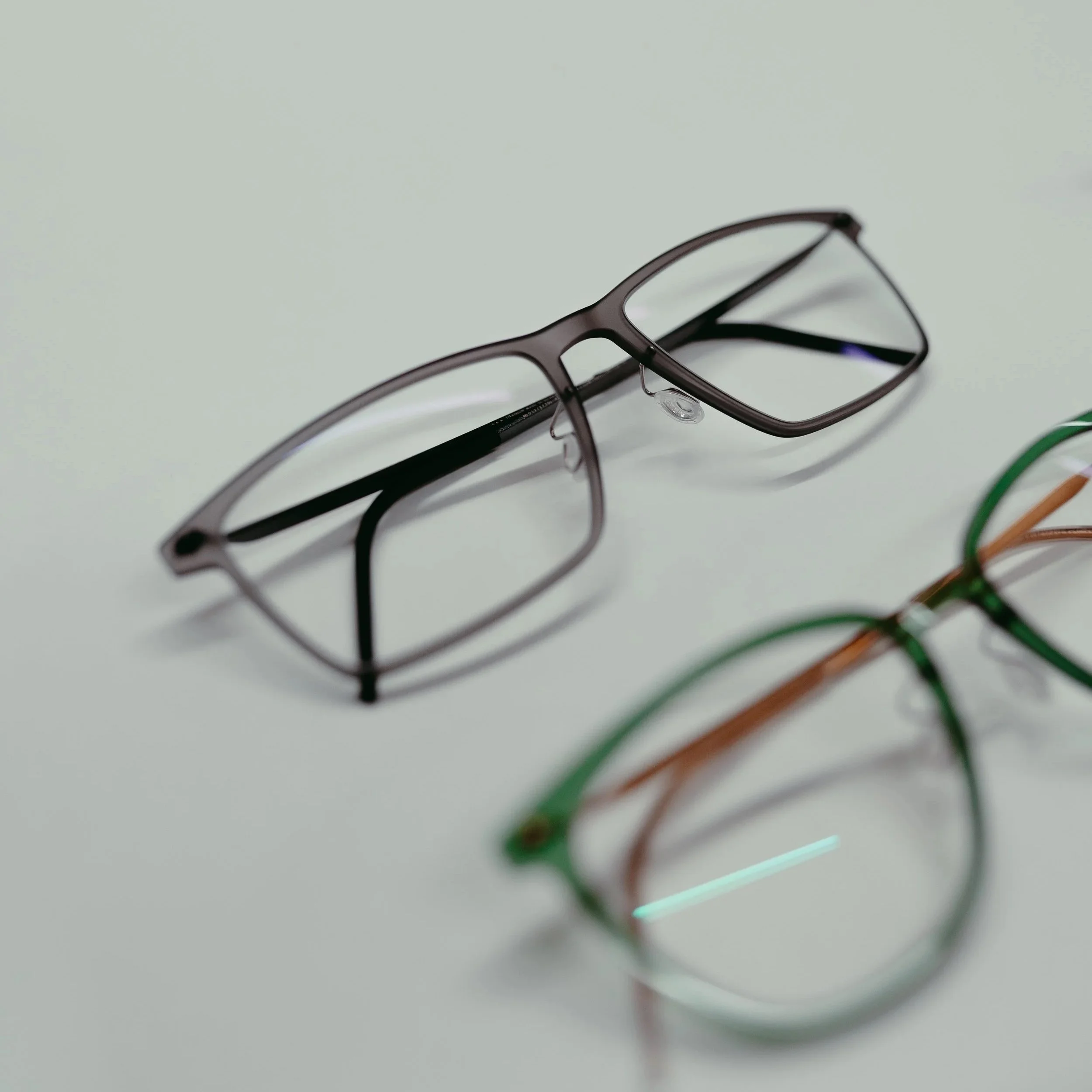 A pair of eyeglasses with black frames resting on a white surface, appearing to be tilted with the right side slightly higher.